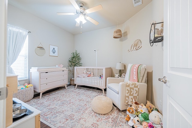 bedroom with a nursery area, visible vents, and ceiling fan