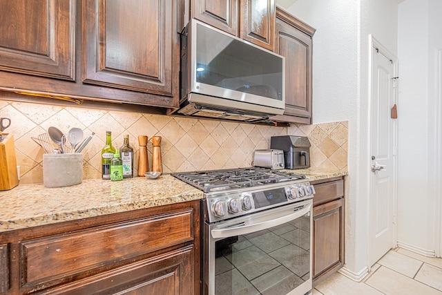 kitchen featuring appliances with stainless steel finishes, light tile patterned flooring, light stone countertops, and decorative backsplash