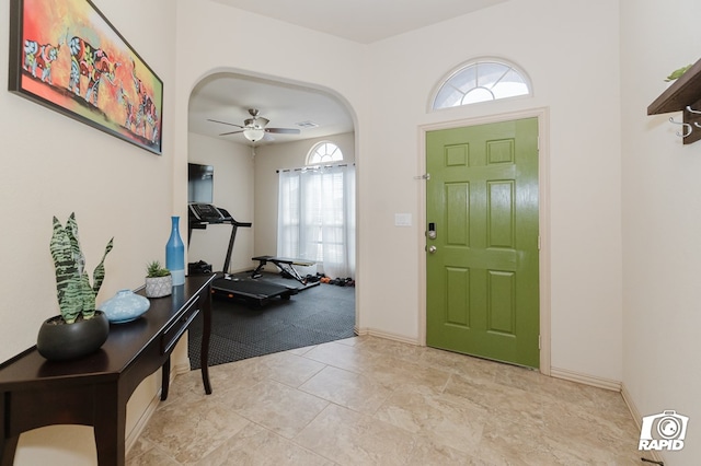 foyer entrance featuring baseboards, arched walkways, and a ceiling fan