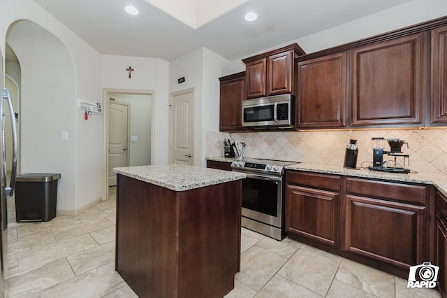 kitchen featuring stainless steel appliances, a center island, light stone counters, and tasteful backsplash