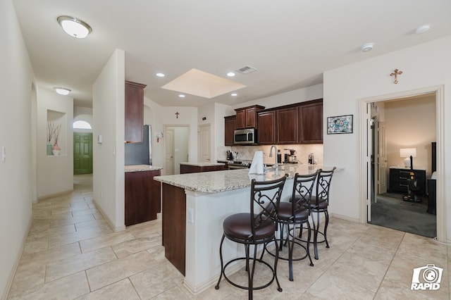 kitchen with a skylight, a breakfast bar area, stainless steel microwave, visible vents, and decorative backsplash