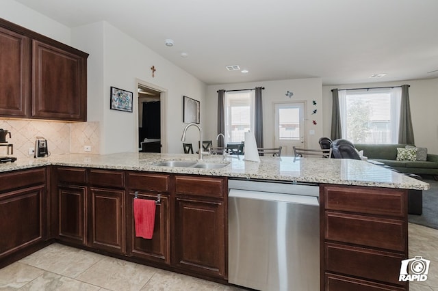 kitchen with light stone counters, a sink, open floor plan, stainless steel dishwasher, and tasteful backsplash