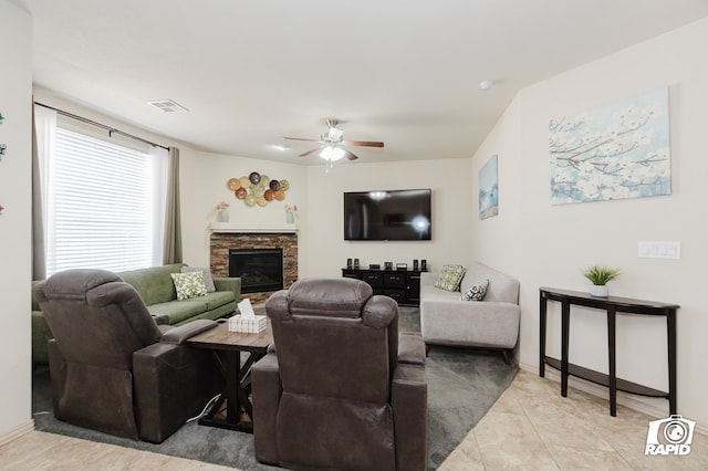 living room with visible vents, a stone fireplace, light tile patterned floors, and a ceiling fan