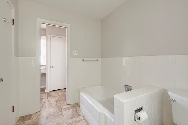 bathroom with a bathtub, toilet, and tile walls