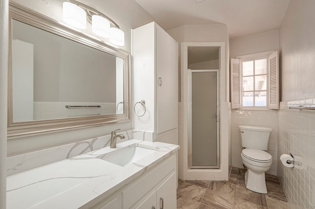 bathroom with vanity, toilet, a shower with door, and tile walls