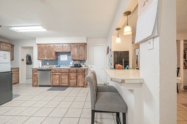 kitchen featuring pendant lighting, dishwasher, backsplash, a textured ceiling, and tile countertops