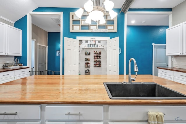 kitchen featuring decorative light fixtures, white cabinetry, sink, and wooden counters