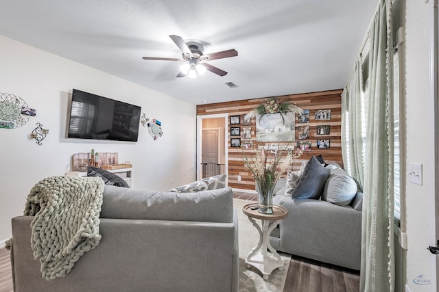 living room featuring wooden walls, ceiling fan, wood-type flooring, and a textured ceiling