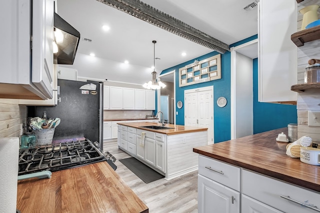kitchen with sink, butcher block countertops, light hardwood / wood-style floors, decorative light fixtures, and white cabinets