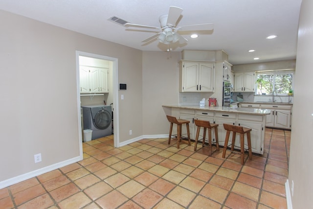 kitchen with tasteful backsplash, a breakfast bar area, white cabinets, kitchen peninsula, and washing machine and dryer