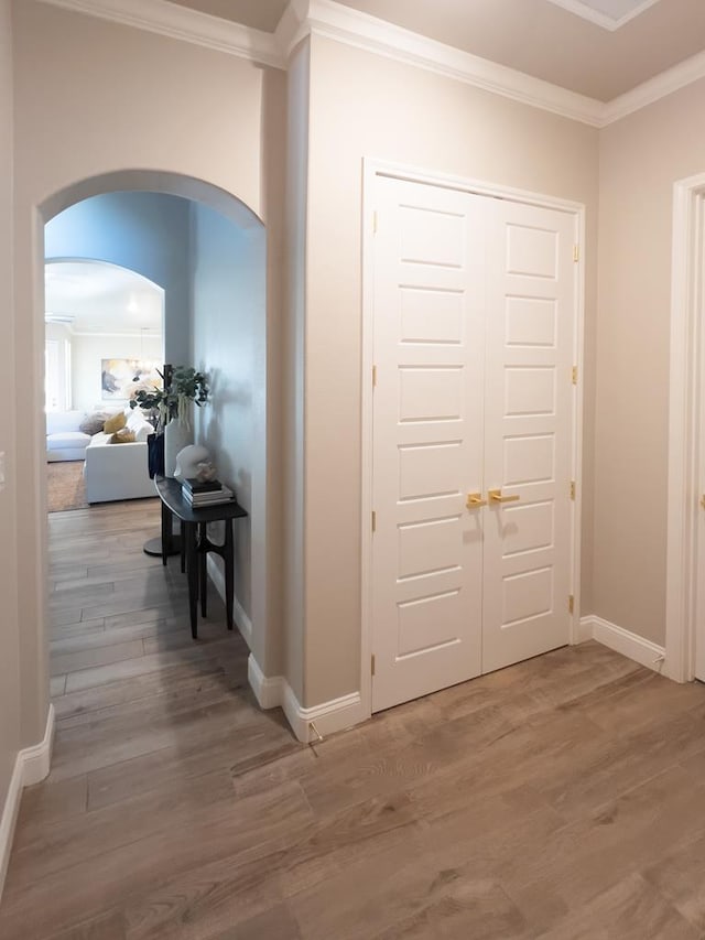 hallway featuring baseboards, arched walkways, crown molding, and wood finished floors