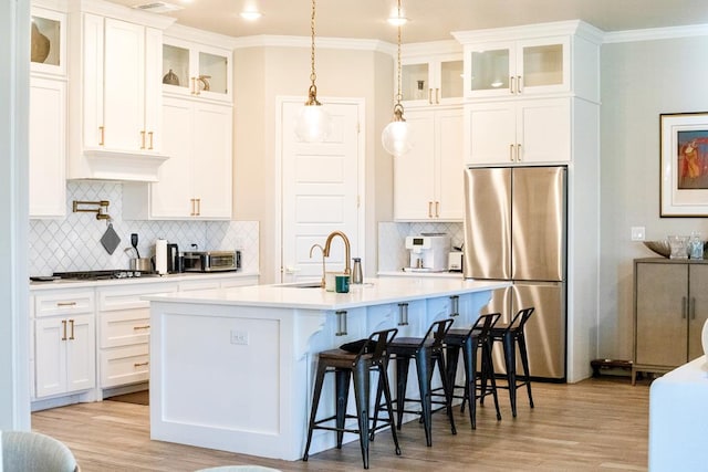 kitchen featuring a kitchen island with sink, a sink, light countertops, appliances with stainless steel finishes, and light wood finished floors