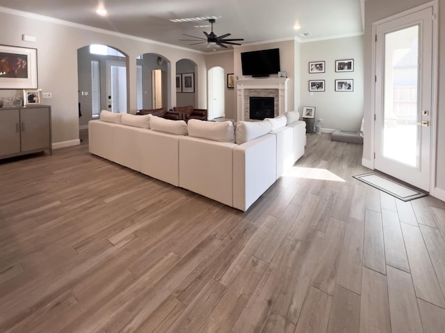 living room with arched walkways, ornamental molding, a fireplace, and light wood-style flooring