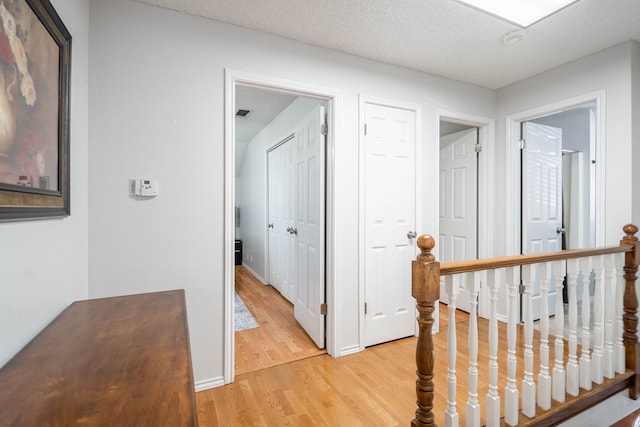 hall featuring light wood finished floors, an upstairs landing, a textured ceiling, and baseboards