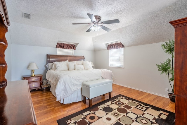 bedroom with visible vents, a textured ceiling, light wood finished floors, baseboards, and vaulted ceiling