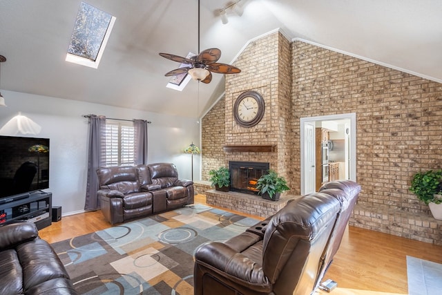 living room featuring wood finished floors, brick wall, a skylight, a fireplace, and ceiling fan