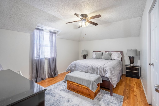 bedroom featuring a textured ceiling, light wood finished floors, baseboards, ceiling fan, and vaulted ceiling