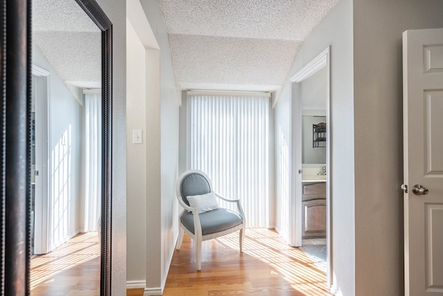 hall with light wood-style floors, a textured wall, and a textured ceiling