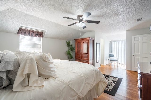 bedroom featuring visible vents, a textured ceiling, light wood-style flooring, and vaulted ceiling