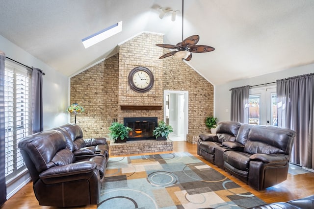 living area with a ceiling fan, wood finished floors, a fireplace, french doors, and lofted ceiling with skylight