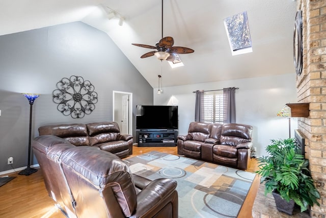 living room with light wood finished floors, a fireplace, a skylight, high vaulted ceiling, and a ceiling fan