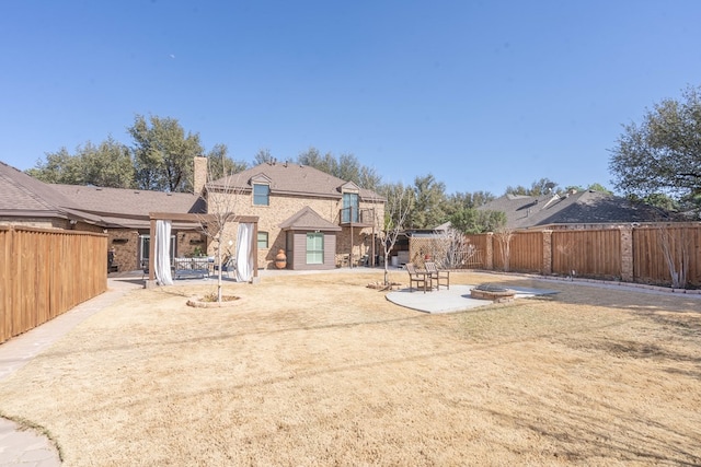 back of house featuring an outdoor fire pit, a lawn, a chimney, a fenced backyard, and a patio