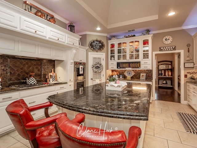 kitchen featuring light tile patterned flooring, a kitchen island, appliances with stainless steel finishes, white cabinetry, and a kitchen bar