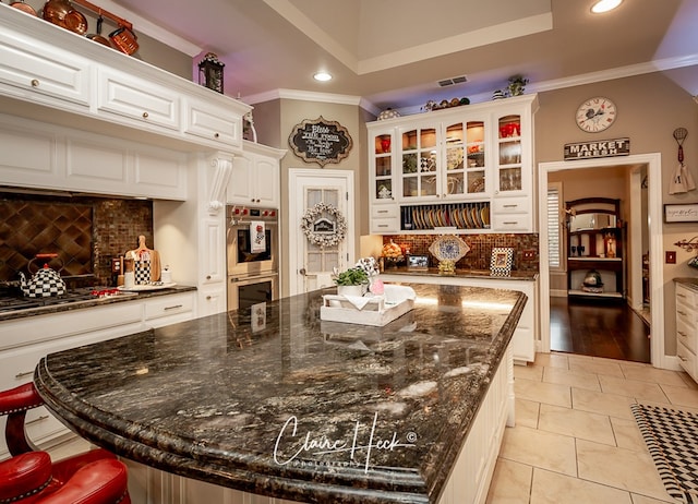 kitchen with white cabinetry, appliances with stainless steel finishes, crown molding, and dark stone counters