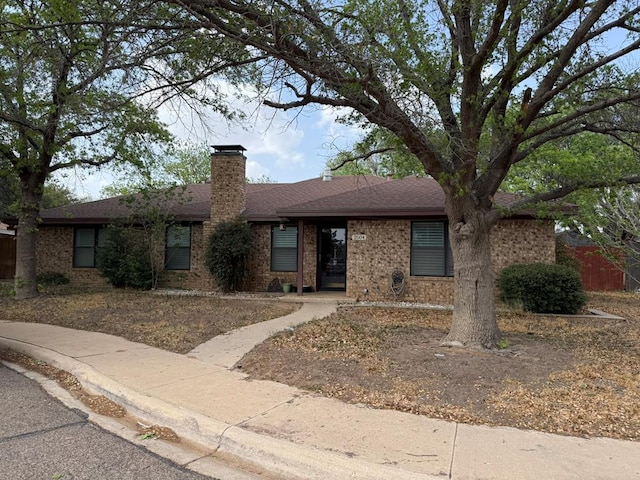 single story home with roof with shingles, a chimney, and brick siding