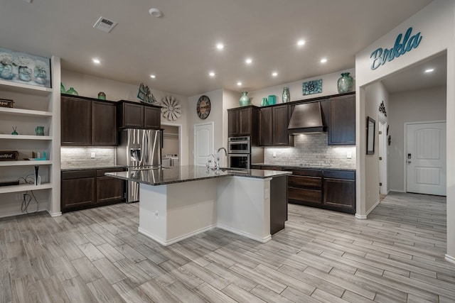 807 Bronco Ct, Midland, TX 79705 - kitchen featuring custom range hood, stainless steel appliances, tasteful backsplash, dark stone counters, and an island with sink