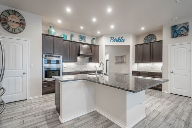 807 Bronco Ct, Midland, TX 79705 - kitchen with wall chimney range hood, wood tiled floors, backsplash, dark stone countertops, and dark brown cabinets