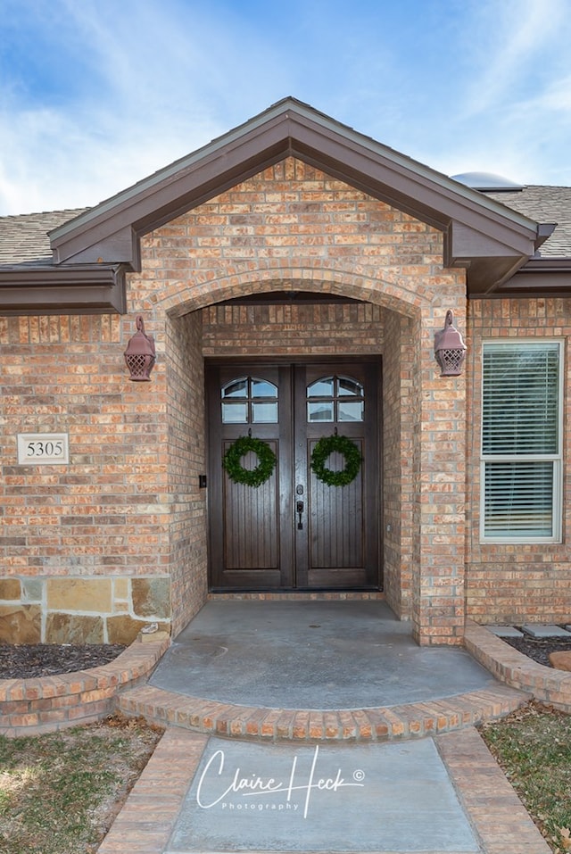 property entrance featuring brick siding and a shingled roof