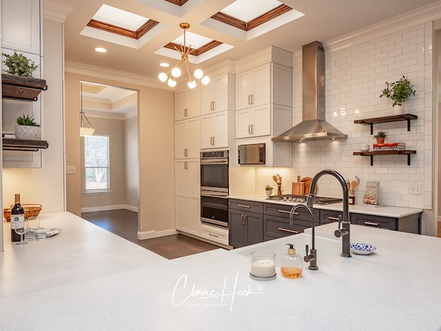 kitchen featuring open shelves, coffered ceiling, appliances with stainless steel finishes, wall chimney exhaust hood, and crown molding