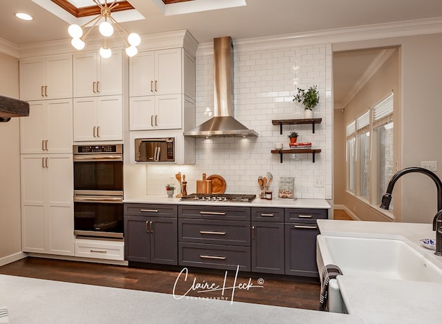 kitchen featuring wall chimney exhaust hood, ornamental molding, dark wood-type flooring, stainless steel appliances, and a sink