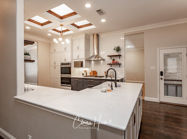 kitchen featuring coffered ceiling, visible vents, wall chimney range hood, appliances with stainless steel finishes, and crown molding