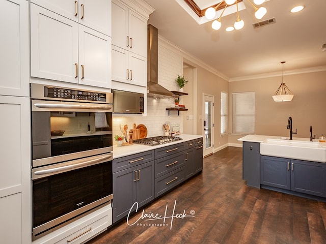 kitchen with visible vents, stainless steel appliances, crown molding, wall chimney range hood, and a sink