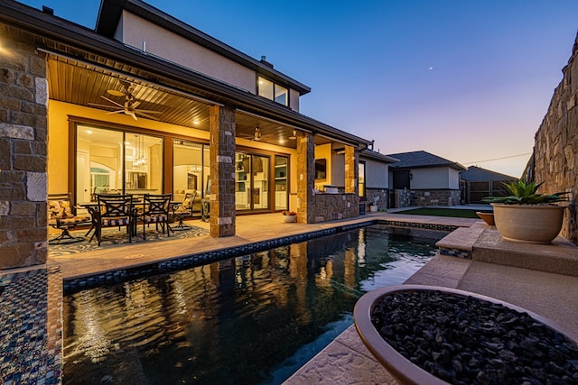 pool at dusk with a patio and ceiling fan