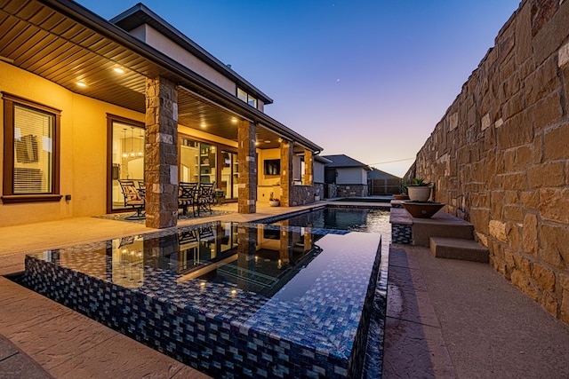 pool at dusk featuring a patio and a jacuzzi