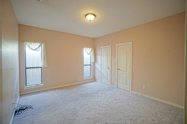 spare room with baseboards and light colored carpet