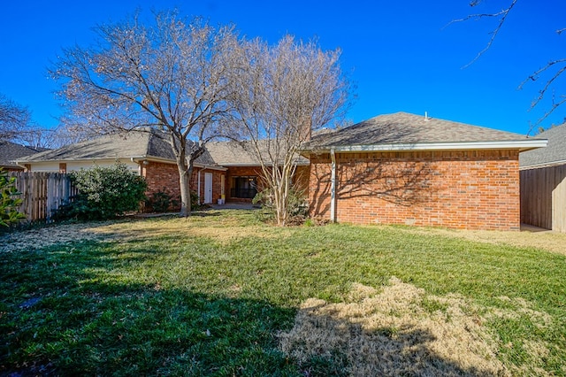 rear view of property featuring brick siding, a yard, and fence