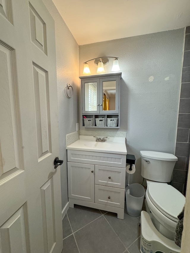 bathroom featuring tile patterned flooring, toilet, vanity, and a textured wall