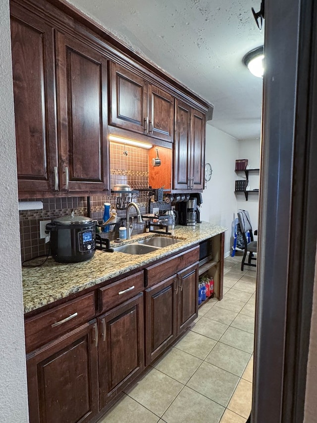 kitchen with a sink, light stone counters, light tile patterned floors, decorative backsplash, and dark brown cabinets