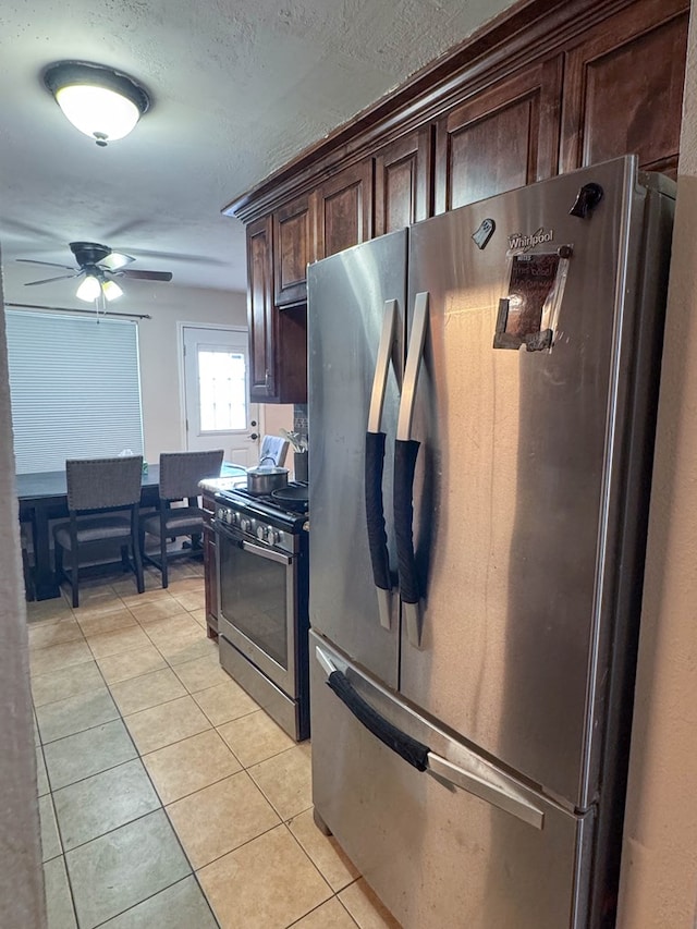 kitchen with a textured ceiling, stainless steel appliances, dark brown cabinetry, light tile patterned floors, and ceiling fan