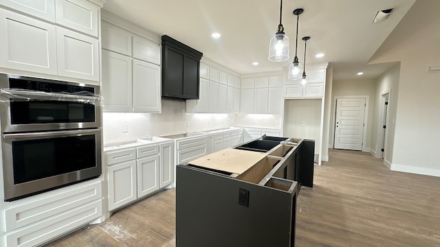 kitchen with light wood finished floors, a center island, double oven, stovetop, and recessed lighting