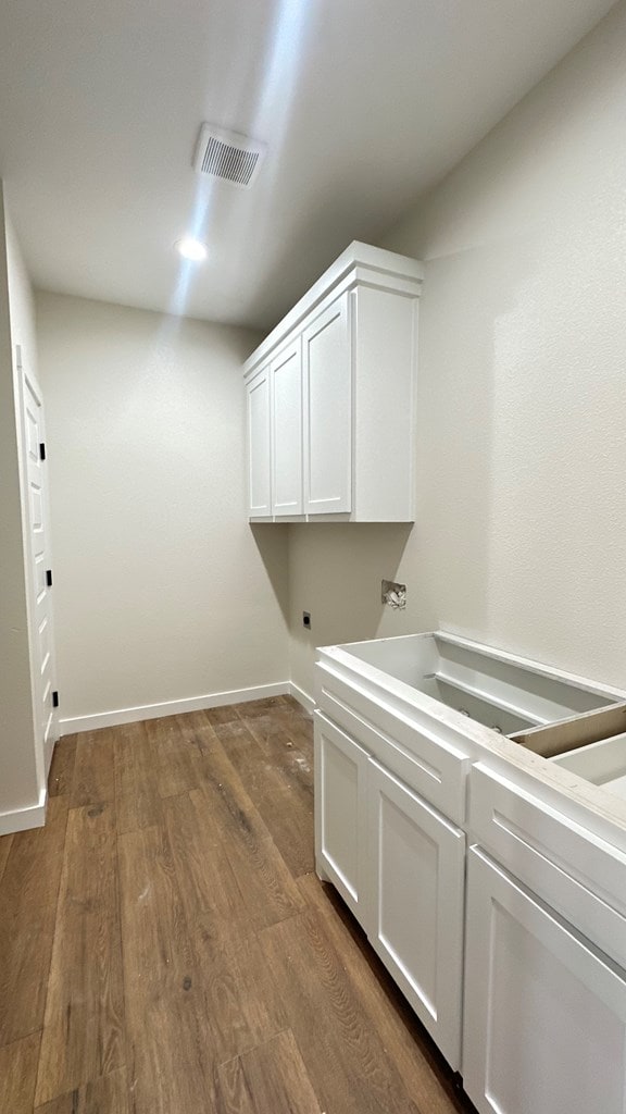 washroom with electric dryer hookup, visible vents, dark wood finished floors, cabinet space, and baseboards