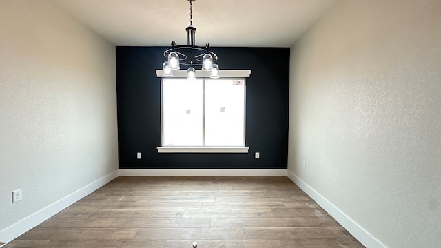 unfurnished dining area with a chandelier, baseboards, and wood finished floors