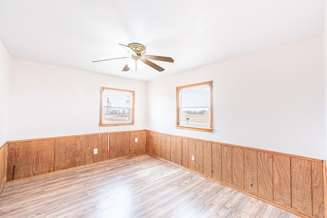 1204 Tinker St, Seagraves, TX 79359 - empty room with light wood-style floors, a ceiling fan, wood walls, and wainscoting