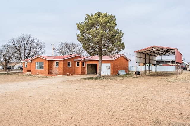 1204 Tinker St, Seagraves, TX 79359 - view of front facade featuring metal roof, brick siding, fence, driveway, and a detached carport
