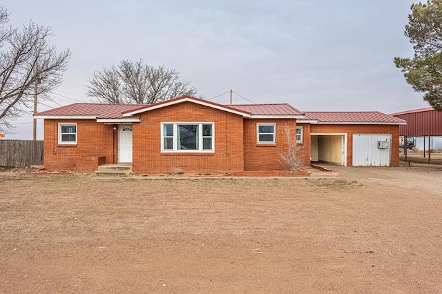 view of front of home featuring brick siding, metal roof, dirt driveway, and fence