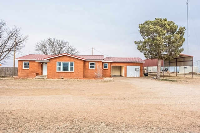 ranch-style house featuring metal roof, brick siding, driveway, and fence